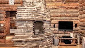 A log cabin interior with a stone fireplace, a wooden door, a mounted television, and a small table with a red cushion.