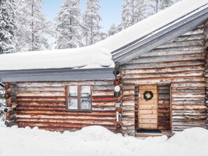 A log cabin with a wooden door and a window, surrounded by snow.
