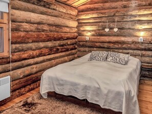 A log cabin room with a bed, a heater, and wall-mounted lights.