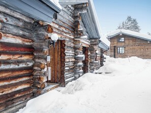 A log cabin with a wooden door and a mailbox, surrounded by snow.