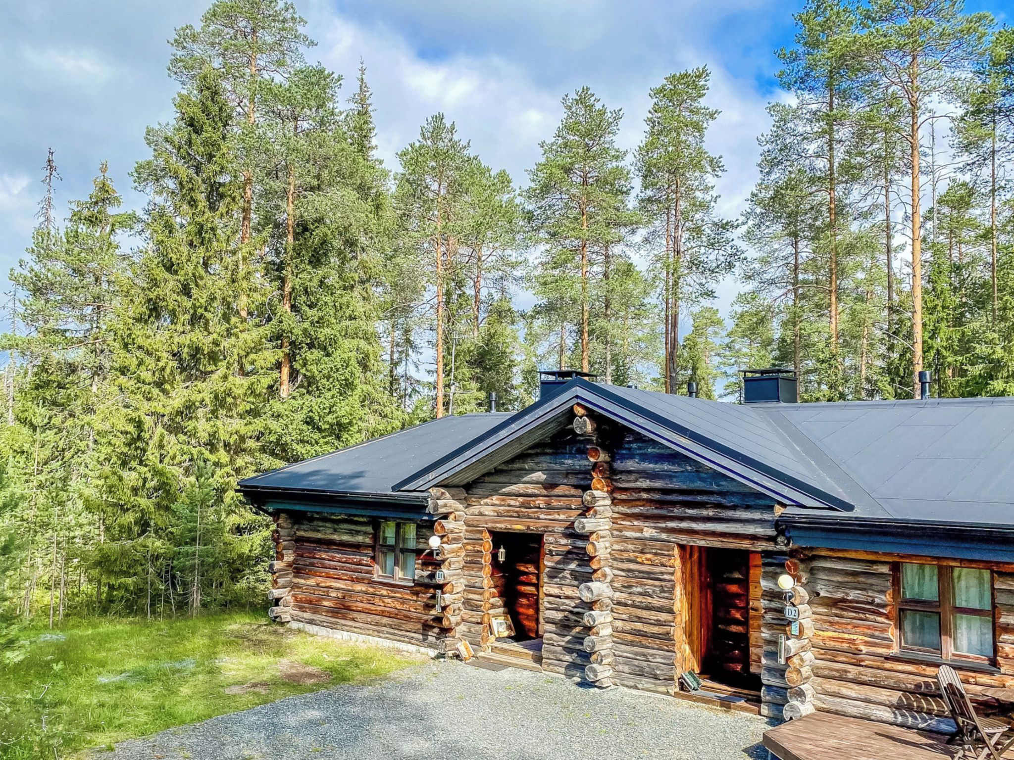A log cabin with a sloped roof, surrounded by a forest.