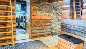 A log cabin interior with a wooden bench, a stone wall, and a door leading to another room.