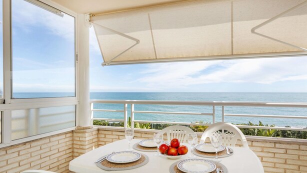 Une table dressée pour deux personnes, avec vue sur la mer, des chaises blanches et une nappe blanche.
