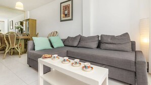 Un salon moderne avec un canapé gris, une table basse blanche et un coin repas comprenant des chaises en osier et un buffet.