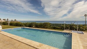 Une piscine rectangulaire à l’eau d’un bleu limpide, entourée d’une terrasse en pierre et d’une haie basse.