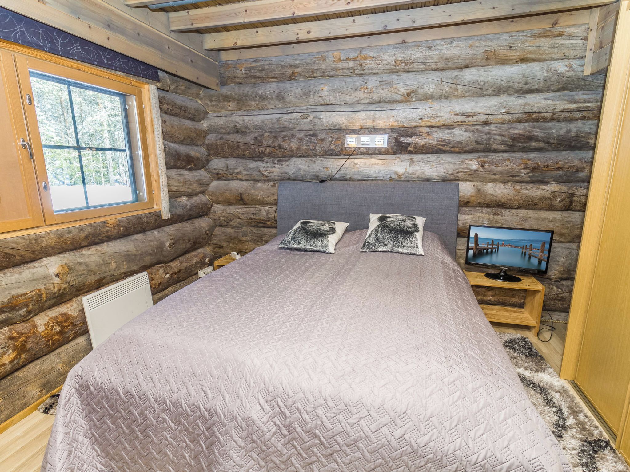 A log cabin bedroom with a bed, pillows, a television, and a window.