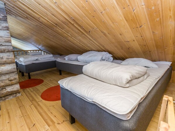 A cozy attic bedroom with two beds, a red rug, and wooden walls.