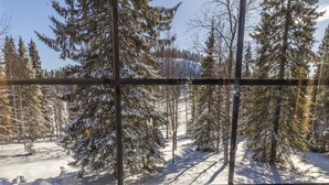 A snowy forest scene through a metal grid.