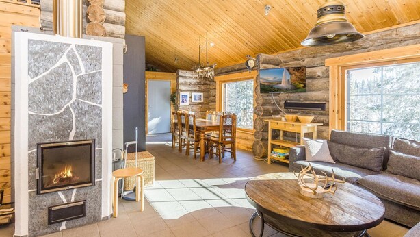 A cozy log cabin interior with a stone fireplace, wooden furniture, and a large window offering a view of the outdoors.