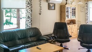 A living room with a sofa, two chairs, a table, and a kitchen area with cabinets and a window. - Långstrands stuga by Interhome (Raasepori)
