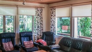 A living room with a leather sofa, two armchairs, a wooden coffee table, and large windows with curtains. - Långstrands stuga by Interhome (Raasepori)