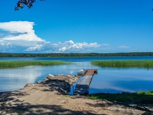 A wooden dock extending into a calm lake with a clear sky and distant forest.
