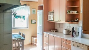 A kitchen with wooden cabinets, a refrigerator, a microwave, a coffee maker, and a dining area with a table and chairs. - Långstrands stuga by Interhome (Raasepori)