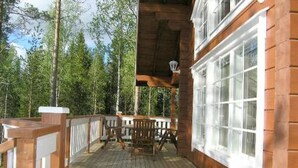 Une terrasse en bois avec une rambarde, une table et des chaises, entourée d’arbres.