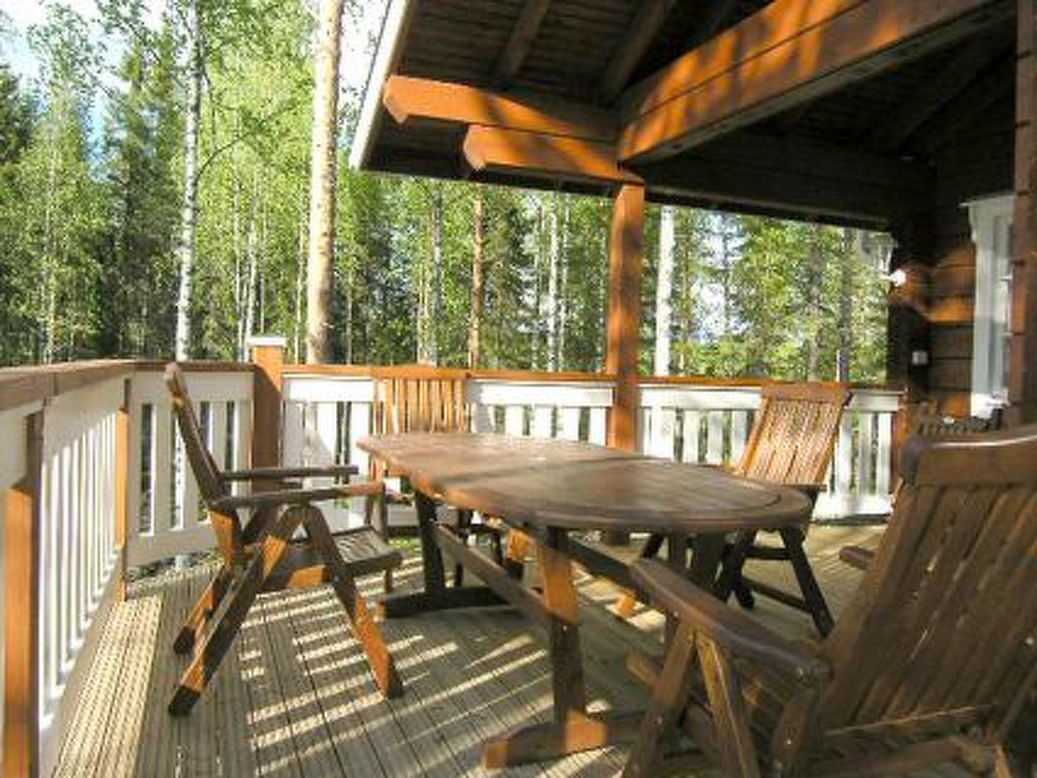 A wooden deck with a table and chairs, surrounded by trees.