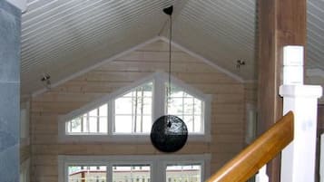 A room with a sloped ceiling, wooden beams, a wooden staircase, and large windows.