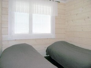 Ein Zimmer mit zwei Einzelbetten, Holzwänden, einem Fenster mit weißen Jalousien und einem schlichten, klaren Design.