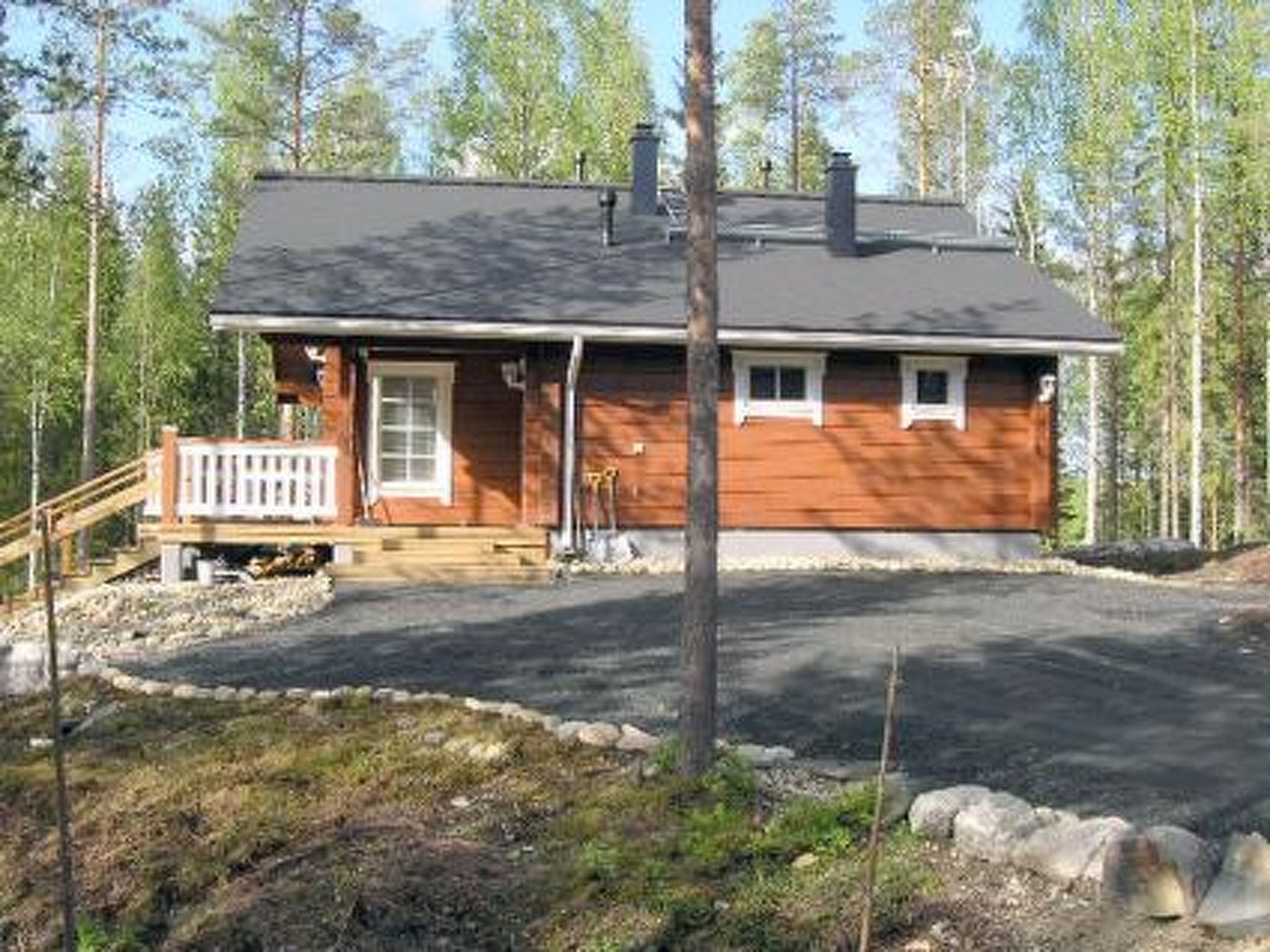 Yhden kerroksen puutalo, jossa on etukuisti, savupiippu ja sisäänkäyntiin johtava ajotie.