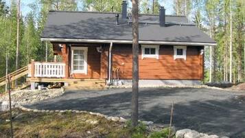 Yhden kerroksen puutalo, jossa on etukuisti, savupiippu ja sisäänkäyntiin johtava ajotie.