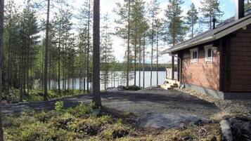 A cabin with a wooden exterior, a porch, and a view of a lake surrounded by tall trees.