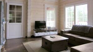 Une pièce avec un intérieur en bois, une porte blanche, un téléviseur posé sur un meuble, un canapé et une petite table.