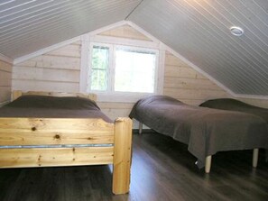 Un dormitorio con techo inclinado, cama de madera, ventana y una pequeña mesa.