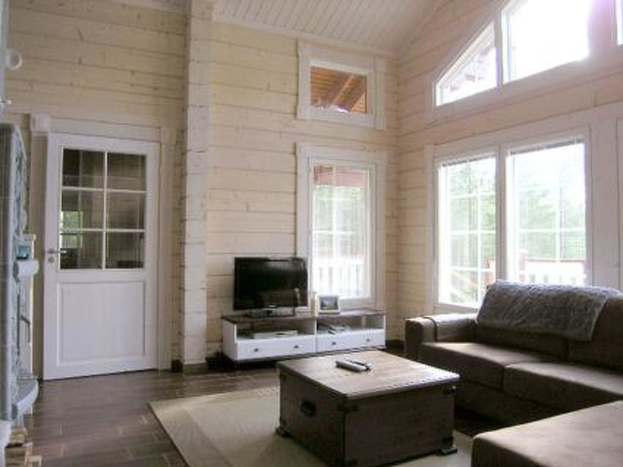 Una habitación con interior de madera, una puerta blanca, un televisor sobre un mueble, un sofá y una mesita.