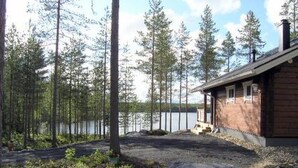 Une cabane avec une façade en bois, une véranda et une vue sur un lac entouré de grands arbres.
