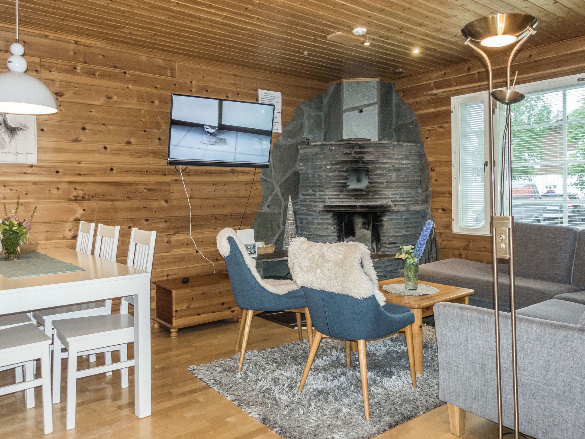 A cozy cabin interior with a stone fireplace, wooden walls, a dining area, and a television mounted on the wall.