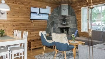 A cozy cabin interior with a stone fireplace, wooden walls, a dining area, and a television mounted on the wall.