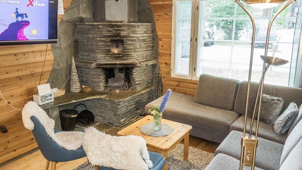L’intérieur chaleureux d’un chalet avec une cheminée en pierre, un téléviseur fixé au mur et un coin salon confortable comprenant un canapé et des fauteuils.