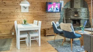 Un salon chaleureux avec une cheminée en pierre, des murs en bois, une table à manger avec des chaises et un téléviseur fixé au mur.