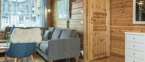 Ein gemütliches Blockhauss-Interieur mit einer Couch, einem Sessel, einer Stehlampe und einem Schminktisch.