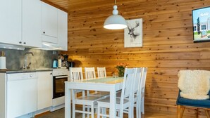 Une cuisine moderne avec des meubles blancs, une table à manger avec des chaises, un luminaire suspendu et un tableau au mur.