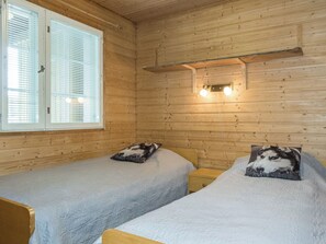 Une chambre avec deux lits, des murs en bois, une fenêtre avec des stores et un luminaire fixé au mur.
