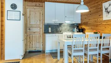 Una cocina con armarios de madera, una mesa de comedor blanca con sillas, una lámpara colgante y un reloj en la pared.