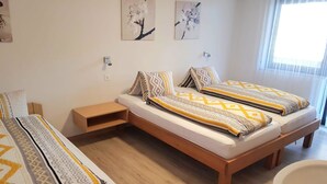 Un dormitorio con dos camas, una mesita de noche, un estante pequeño y un ventanal grande.