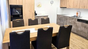 Una cocina moderna con armarios de madera, horno empotrado y comedor con mesa de madera y sillas negras.