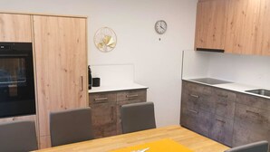 Una cocina moderna con armarios de madera, horno empotrado, lavamanos y zona de comedor con mesa y sillas.