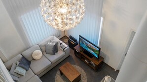 Ein modernes Wohnzimmer mit einer großen Couch, einem Couchtisch, einem Fernseher auf einem Holzgestell und einem außergewöhnlichen kugelförmigen Kronleuchter.