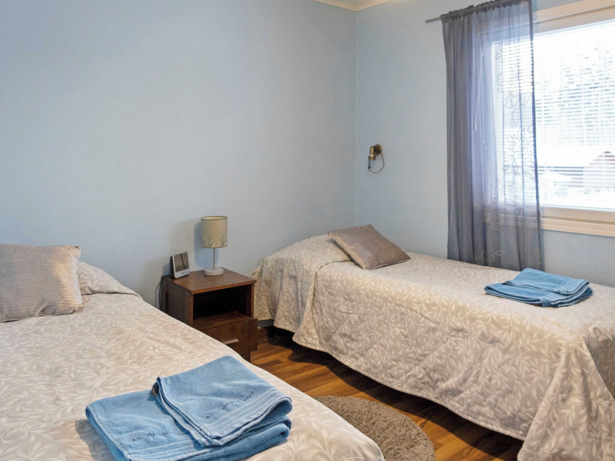 A bedroom with two beds, a nightstand, a lamp, and a window with curtains.