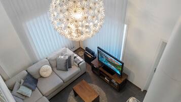 Een moderne woonkamer met een grote flatscreen televisie, een grijze bank, een houten salontafel en een bijzondere bolvormige kroonluchter.