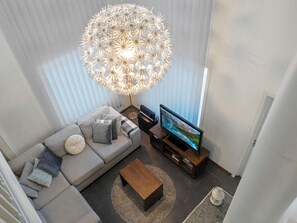 Een moderne woonkamer met een grote flatscreen televisie, een grijze bank, een houten salontafel en een bijzondere bolvormige kroonluchter.