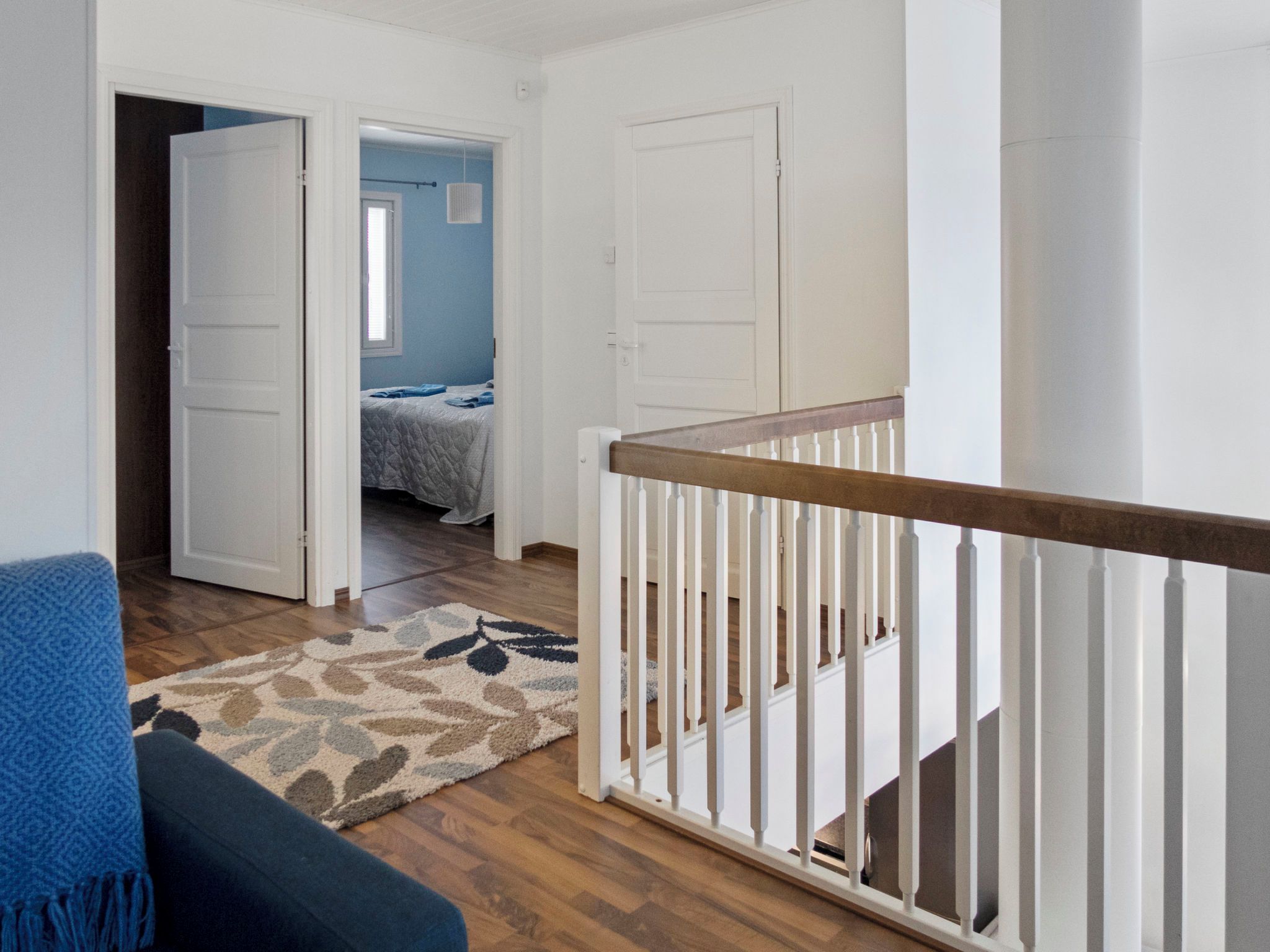 A room with a wooden floor, a blue chair, a white door, and a staircase with a white railing.