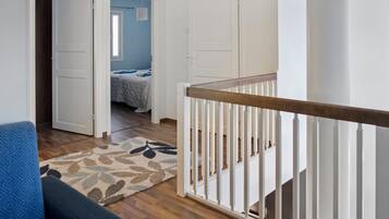 A room with a wooden floor, a blue chair, a white door, and a staircase with a white railing.