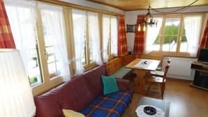 A cozy living room with a red sofa, a wooden dining table, and a television. - Apartment Bolgen by Interhome (Zweisimmen)