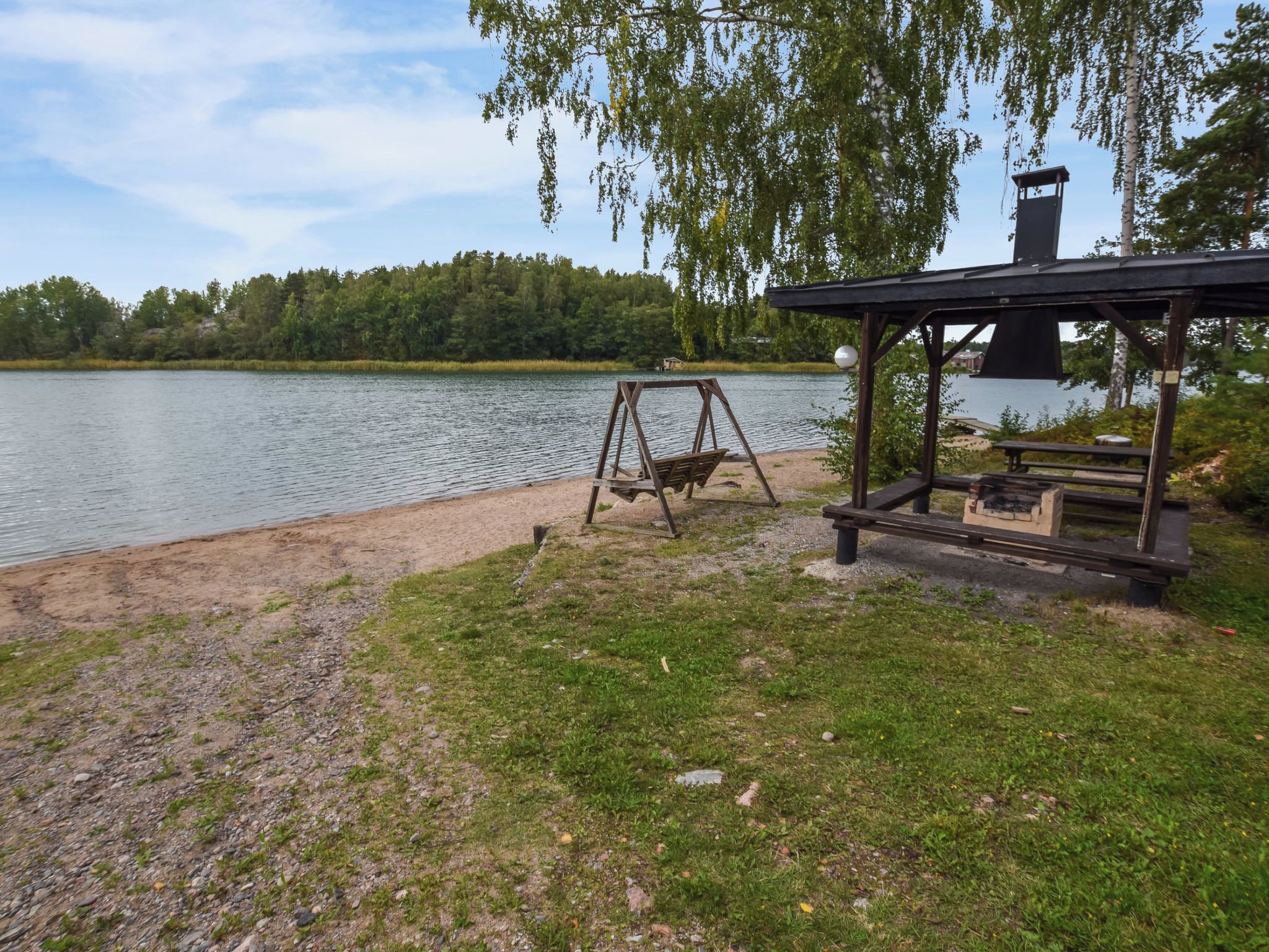Un parc a la vora del llac amb cadira d'oscil·lació, taula de picnic i una glorieta.