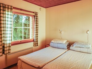 A room with two beds, a window with curtains, a radiator, and a wall-mounted light fixture. - Isokoskelo 5 by Interhome (Parainen)