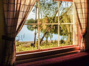 A window with curtains, a view of a lake, and a dock with boats. - Isokoskelo 5 by Interhome (Parainen)