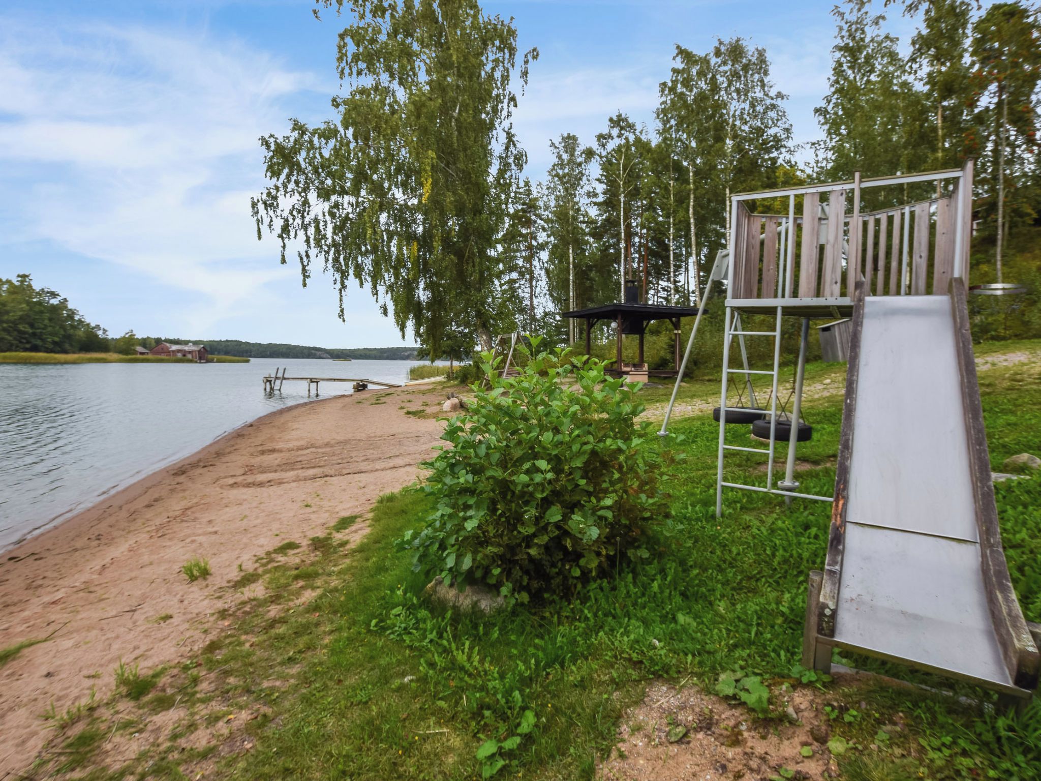 Kaunis paikka järven rannalla, jossa on puinen terassi, liukumäki ja huvimaja.